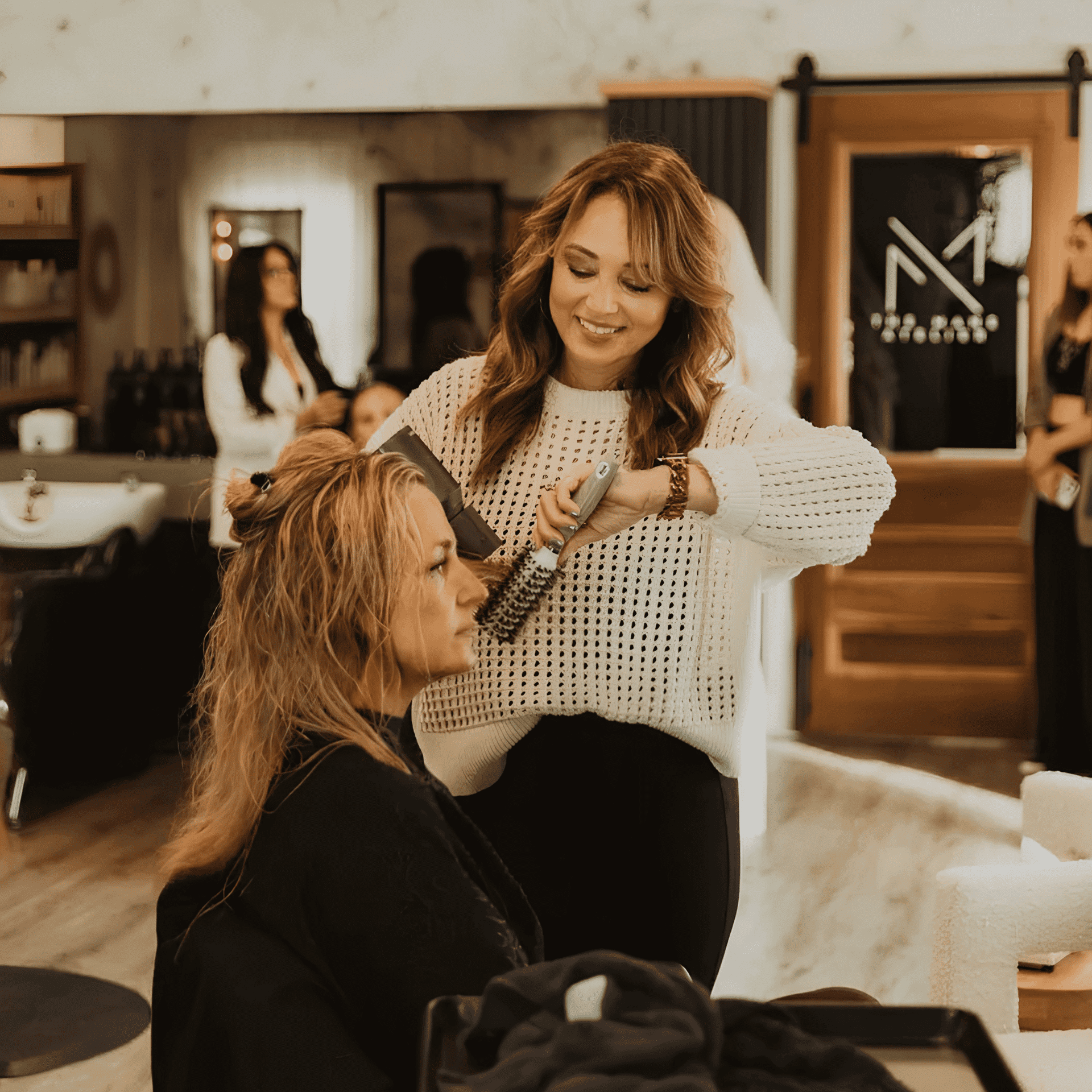 Hairdresser smiling while styling a client's hair in a cozy salon.