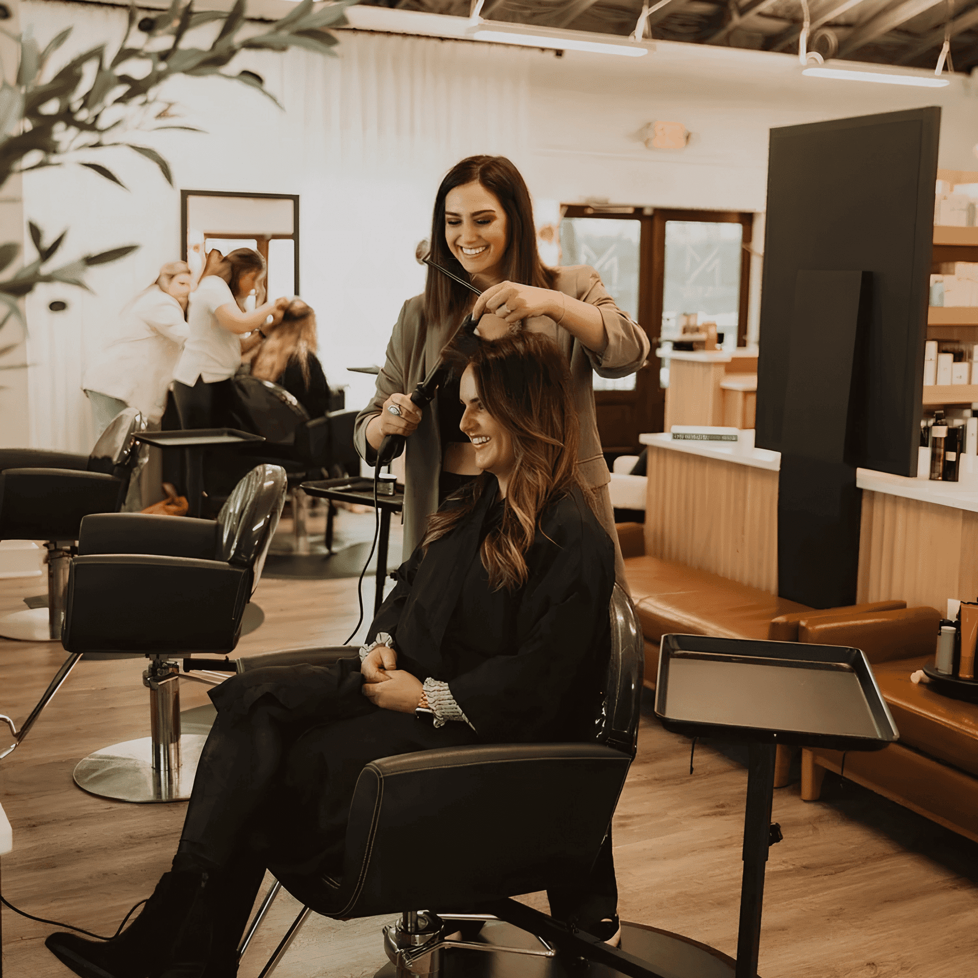 Hairstylist curling a smiling client's hair in a modern salon.